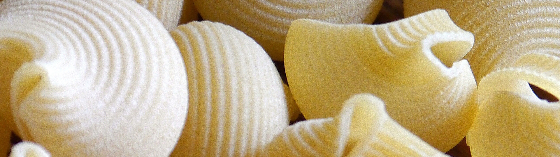 Verschiedene Sorten getrockneter Pasta, darunter Spaghetti und Fusilli, kunstvoll auf einem rustikalen Holztisch arrangiert – ideal für klassische Nudelgerichte.