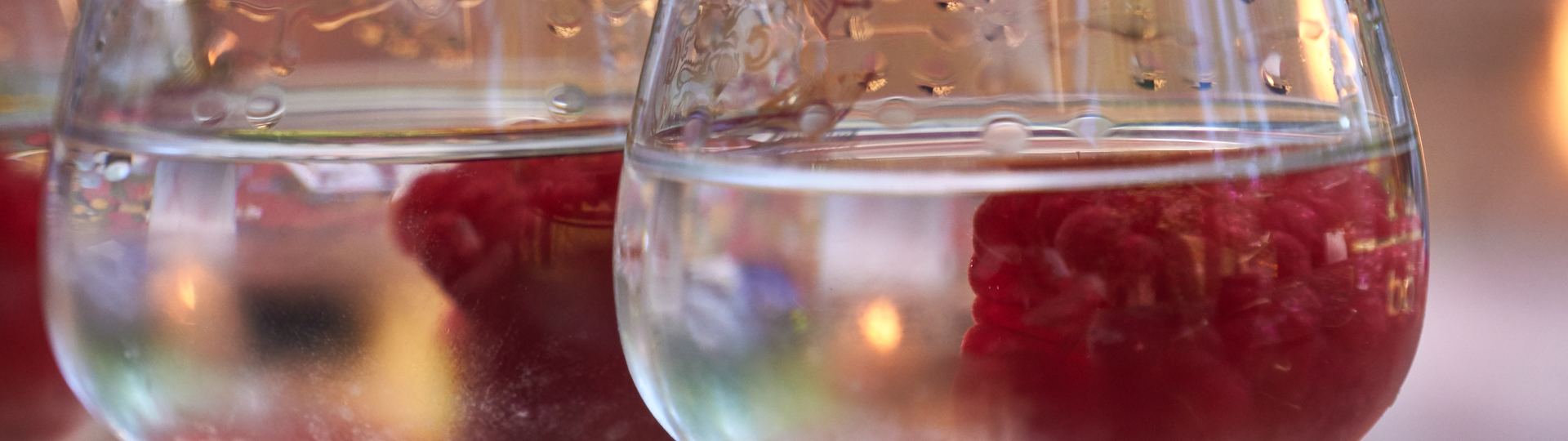 Glas gefüllt mit klarem Himbeergeist und frischen Himbeeren, elegant präsentiert vor einem rustikalen Hintergrund, symbolisierend die Frische und Qualität des edlen Obstbrands.